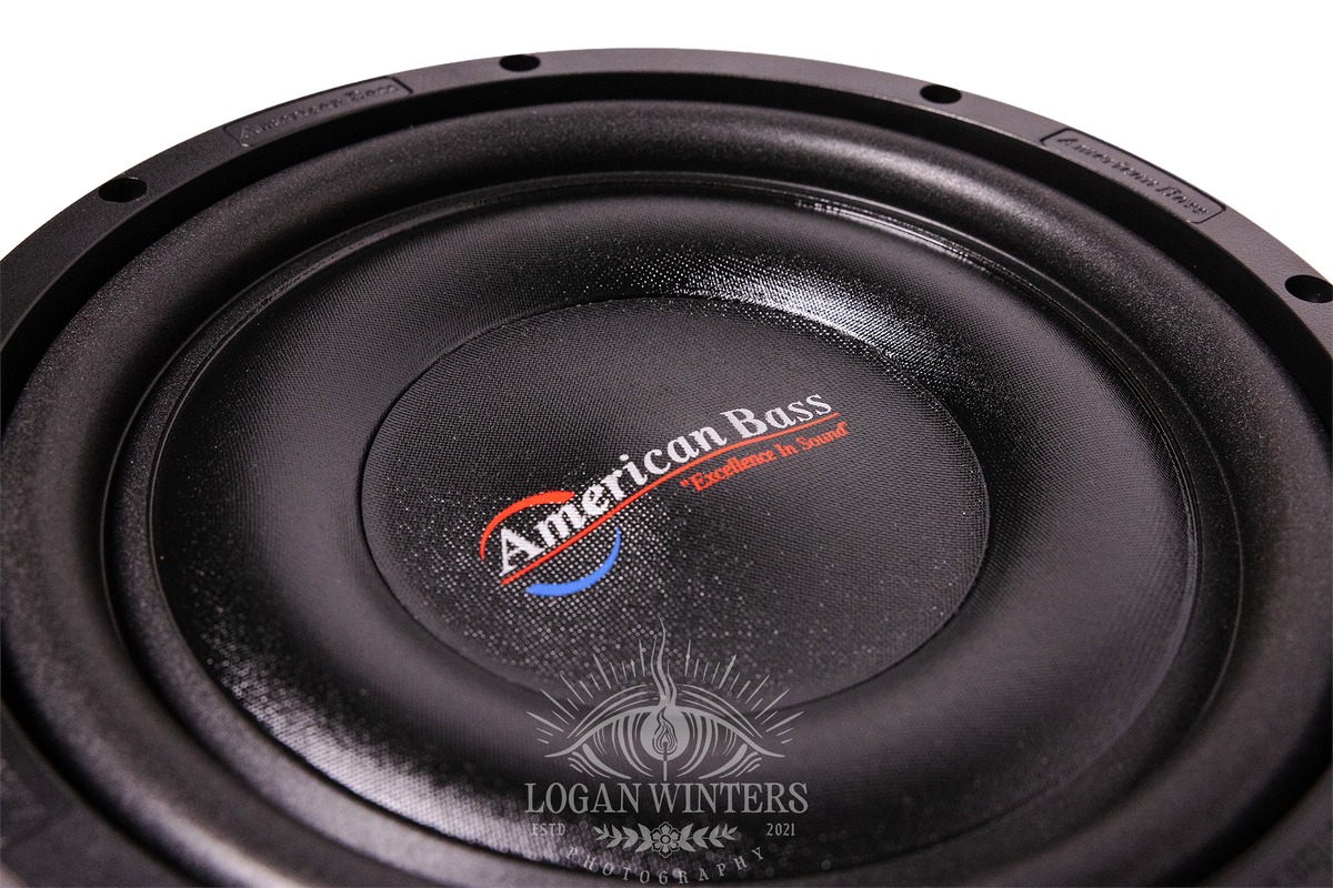 Close-up of an American Bass SL 10″ Car Subwoofer (300 Watts RMS, Single Voice Coil 4 Ohm, Shallow Mount) in black, with the logo and the “Excellence in Sound” slogan visible at the center, photographed by Logan Winters.
